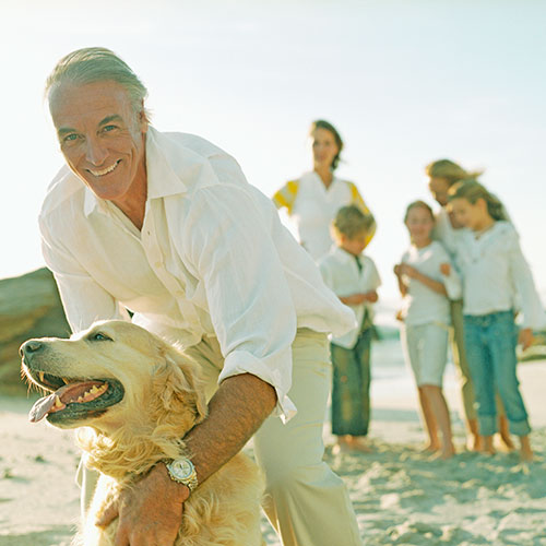 Mature Man Embracing Golden Retriever Dog with Family at Beach