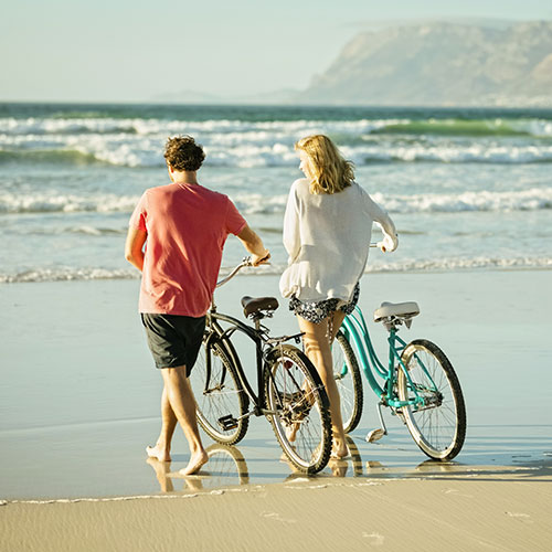 Couple Standing By Their Bikes Heading Down Beach Shoreline